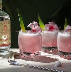 three glasses filled with pink liquid sitting on top of a table next to a bottle