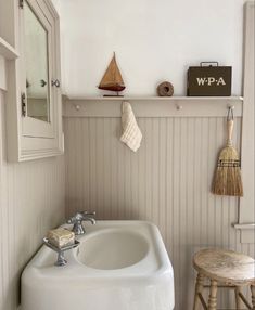 a white sink sitting under a bathroom mirror next to a wooden stool and wall hanging