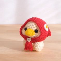 a small crocheted bird with a red scarf around it's neck sitting on a wooden surface