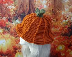 an orange knitted hat on top of a mannequin's head in front of a tree