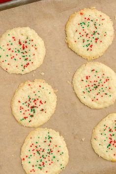 six cookies with sprinkles are on a baking sheet, ready to be baked