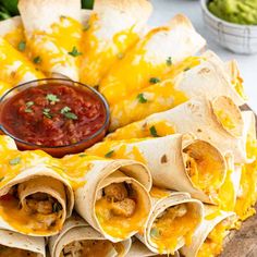 several burritos on a wooden platter with salsa and guacamole