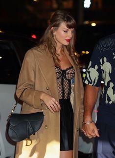 a man and woman holding hands while walking down the street at night with cars behind them