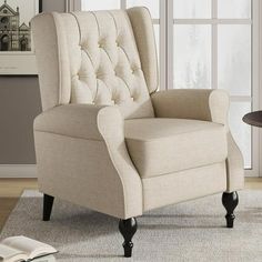 a beige chair sitting in front of a window next to a table with a book on it