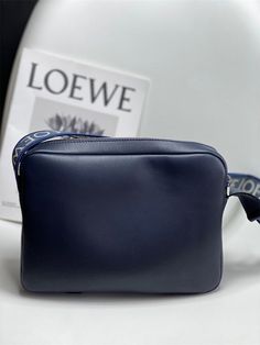 a small blue purse sitting on top of a white table next to a sign that says loewe