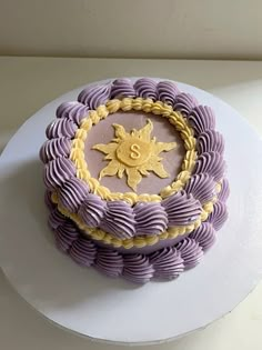 a purple and yellow decorated cake sitting on top of a white plate with gold decorations