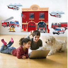 two children laying on the floor with a dog and laptop in front of fire station wall decals