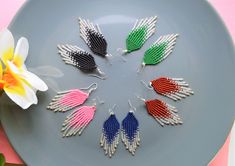 six pairs of beaded earrings sitting on top of a plate next to a flower