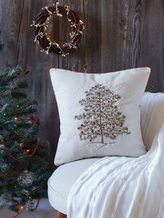 a christmas tree pillow sitting on top of a white chair next to a christmas tree