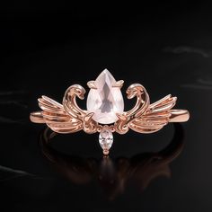 a rose gold ring with an angel wing design and a pear shaped diamond on the side