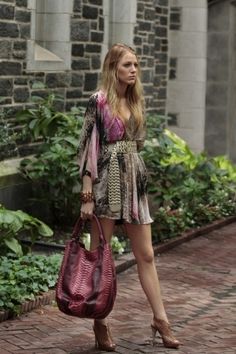 a woman is walking down the street carrying a handbag in her right hand and looking off into the distance