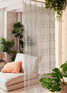 a living room filled with lots of plants next to a white couch covered in sheer curtains