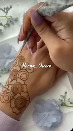 a woman is doing henna on her arm with a pen and flower pattern in the background