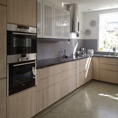 a kitchen with wooden cabinets and black counter tops, an oven in the middle is next to a window