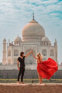 a man and woman standing in front of a white building with a red dress on