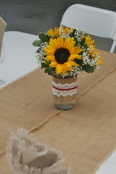 a vase with sunflowers and baby's breath sits on a burlap table runner