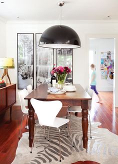 a dining room table with flowers in a vase on it and two people walking by