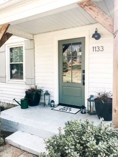 the front door of a house with potted plants on the porch and steps leading up to it