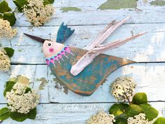 a bird made out of wood sitting on top of some white and green leaves next to flowers