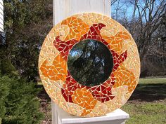 a circular mirror sitting on top of a white pillar next to a tree and grass