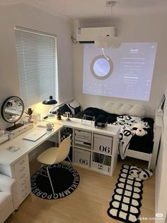 a room with a bed, desk and computer monitor on the wall next to it