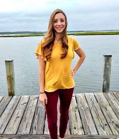 a woman is standing on a dock by the water wearing red pants and a yellow shirt