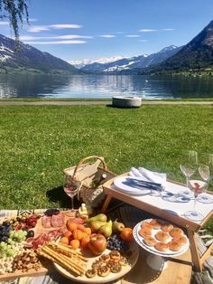 a picnic table with food and wine in front of a lake on a sunny day