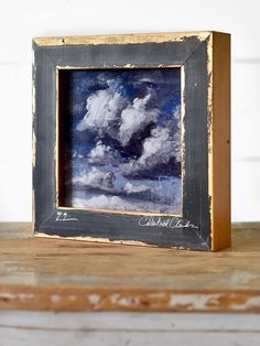 an old photo frame with clouds in the sky on a wooden table next to a white brick wall