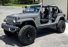 a gray jeep parked in front of a building with its doors open and the door ajar