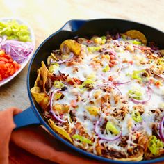 a skillet filled with taco salad and tortilla chips on top of a wooden table