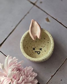 a small bowl with a face drawn on it next to a pink flower