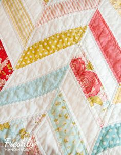 a close up of a quilt on a bed with flowers and stripes in the background