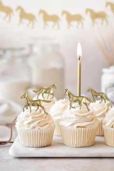 three cupcakes with white frosting and gold horses on them, one has a candle in the middle