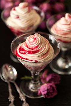 two desserts with whipped cream and raspberries in small glass dishes on a table