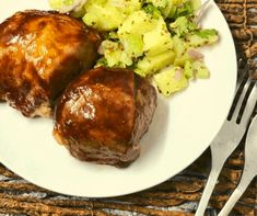 two pieces of meat sitting on top of a white plate next to potatoes and broccoli