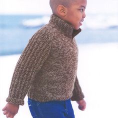 a young boy wearing a brown sweater and blue jeans standing in the snow with his hand on his hip