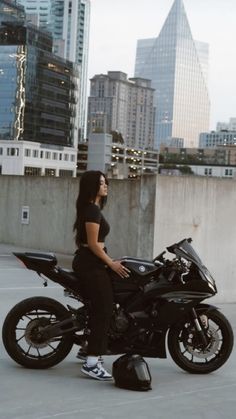 a woman sitting on top of a motorcycle in front of some tall buildings and skyscrapers