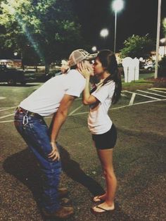 a man kissing a woman on the cheek while standing in a parking lot at night