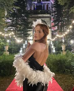 a woman in a black and white feathered dress on a red carpet at night