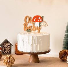 a white cake sitting on top of a table next to pine cones and small trees