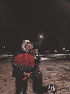 a man and woman dressed in black are kissing on the street at night with red roses