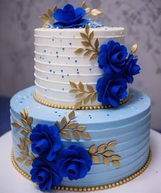 a three tiered cake with blue flowers on the top and gold leaves on the bottom