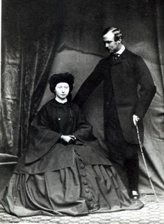 an old black and white photo of a man standing next to a woman in a long dress