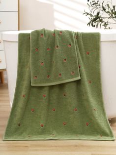 a green blanket with red flowers on it sitting in front of a bathtub next to a potted plant