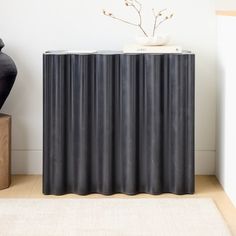 a black cabinet sitting next to a vase on top of a wooden table in front of a white wall