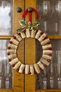 a wreath made out of wine corks on top of a wooden cabinet next to glasses