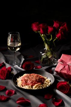 a plate of spaghetti and red roses with a glass of wine on the table next to it