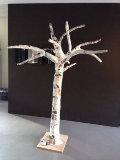 a tree made out of newspaper is shown in front of a black wall and gray floor