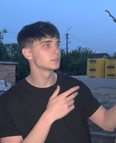 a young man standing in front of a bird flying over his shoulder and looking up at the sky