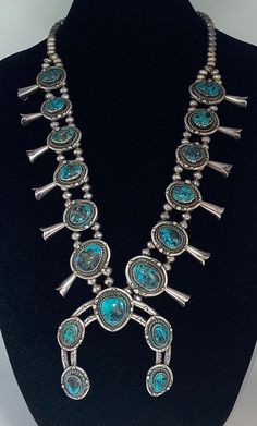 Absolutely stunning Native American handmade squash blossom necklace is made of sterling silver and has natural turquoise stones from the Turquoise Mountain Mine. There are 156 sterling silver beads, 96 of them are in double rows (59 on each side) and 38 of them are in single rows (19 on each side). There are 12 sterling silver squash blossoms, each with a single turquoise stone. In the center of the necklace is a large Naja with 5 turquoise stones. The stones are all a gorgeous vivid blue color with brown and black matrix. Condition: Excellent! Minor wear consistent with age and use  Artist: Unknown/Unsigned  Weight: 295 grams  Measurements: 28 1/2 inches long *156 Sterling Silver Beads: 8mm x 5mm each *12 Squash Blossoms: Vary in size from: 1 3/4 inches long x 1 inch wide to 2 inches lon Turquoise Jewelry Native American Squash Blossom, Silver Squash Blossom Necklace, Squash Blossoms, Natural Turquoise Stone, Southwest Jewelry, Squash Blossom Necklace, Squash Blossom, Turquoise Stones, Natural Turquoise